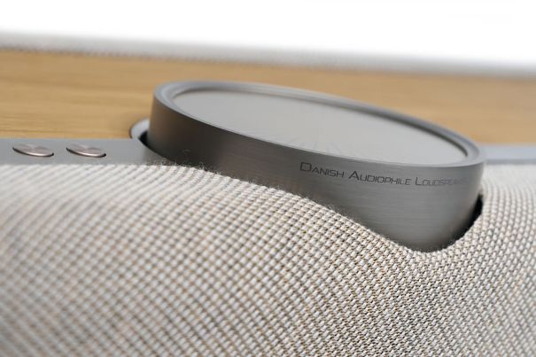 Materialdetail des Dali Vega: das gebürstete Aluminium-Lautstärkerad mit eingraviertem Schriftzug «Danish Audiophile Loudspeakers», daneben die metallenen Bedientasten auf feinem Gewebe.