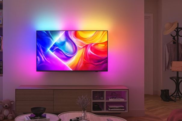 Ein moderner Philips TV mit aktiviertem Ambilight-Effekt – weiches Licht strahlt in mehreren Farben auf eine weisse Wand.